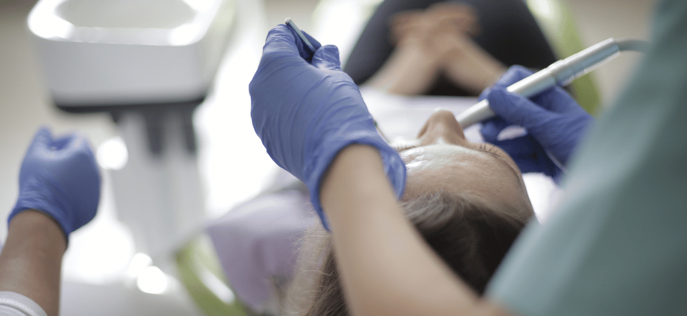 tandläkare utför tandlagning på en patient Tandläkare i blå handskar utför tandlagning på en patient som ligger i en tandläkarstol.